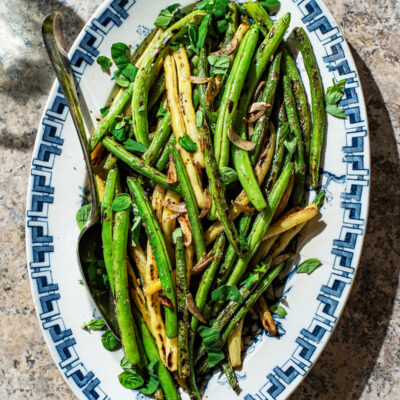 A blue and white platter filled with cooked green and yellow beans with garlic.