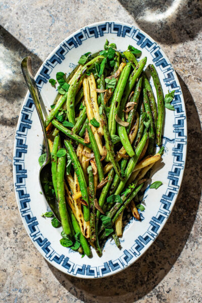 A blue and white platter filled with cooked green and yellow beans with garlic.