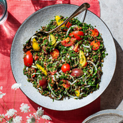 Serving bowl of lentil tabbouleh with cherry tomatoes and onion.