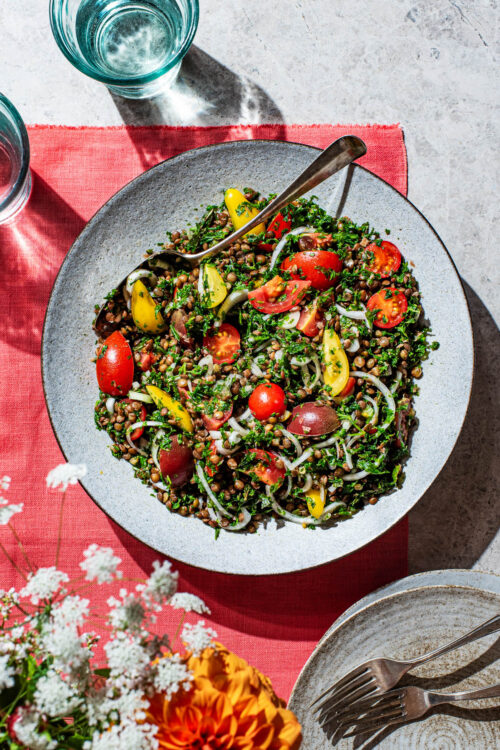 Serving bowl of lentil tabbouleh with cherry tomatoes and onion.