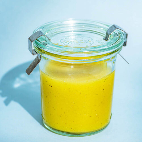 Vinaigrette in a small glass jar with a lid on a blue background.