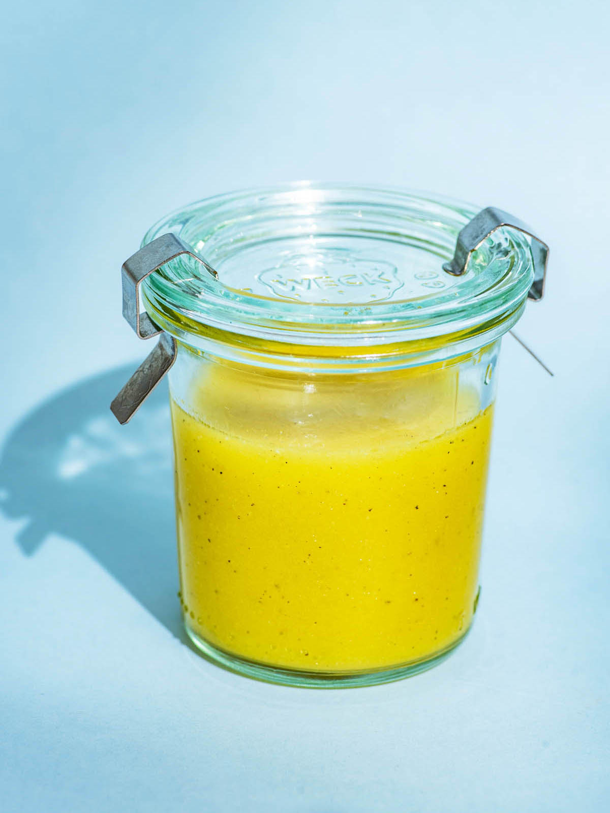 Vinaigrette in a small glass jar with a lid on a blue background.