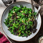 A large serving bowl with a two-colour kale salad topped with dried cranberries and seeds.