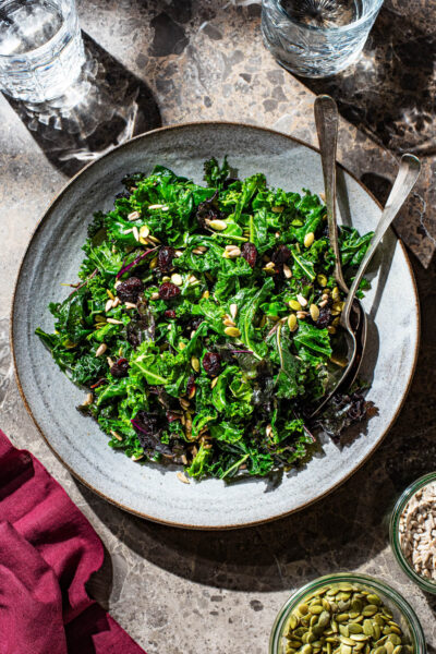 A large serving bowl with a two-colour kale salad topped with dried cranberries and seeds.