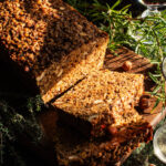 Sliced vegan roast on a cutting board with herbs around.