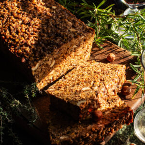 Sliced vegan roast on a cutting board with herbs around.