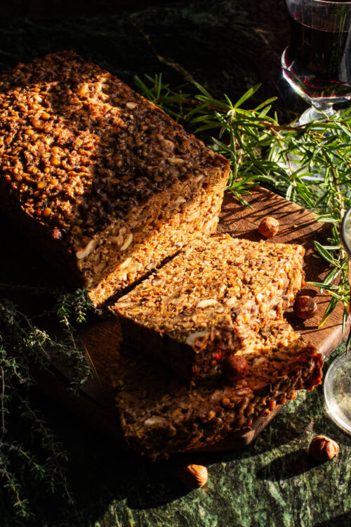 Sliced vegan roast on a cutting board with herbs around.