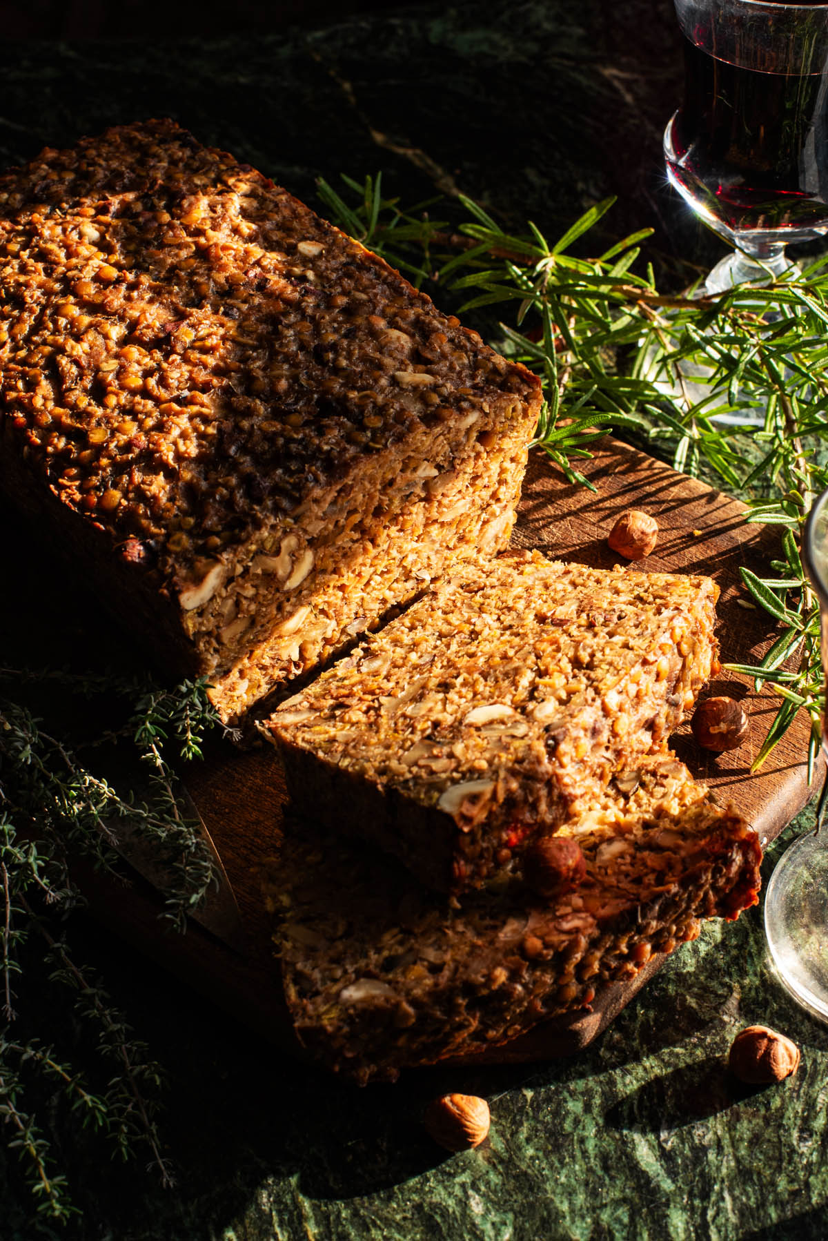 Sliced vegan roast on a cutting board with herbs around.