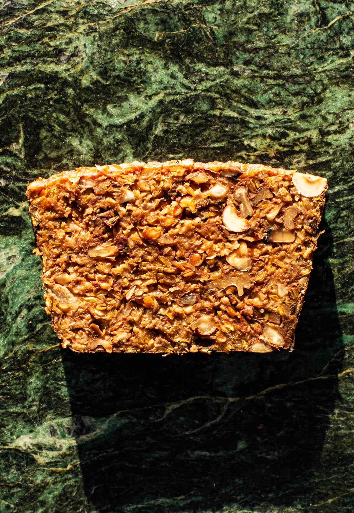 Slice of lentil loaf, top down view, on a green marble background.