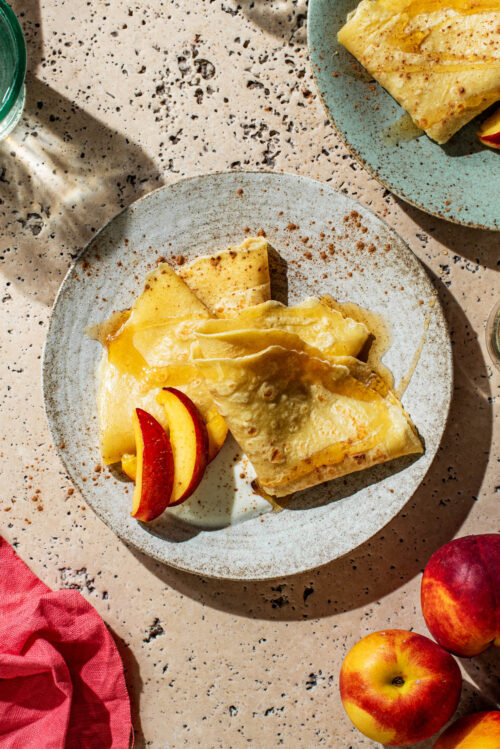 Two flat pancakes folded into triangles on a plate with fruit and yogurt.