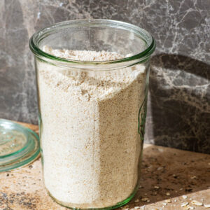A glass jar full of oat flour, with rolled oats around.