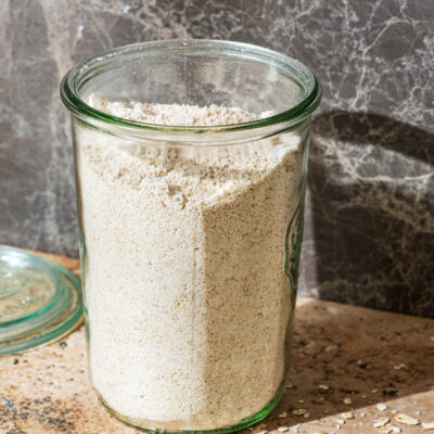 A glass jar full of oat flour, with rolled oats around.