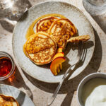 Small pancakes on a plate with fruit and maple syrup.