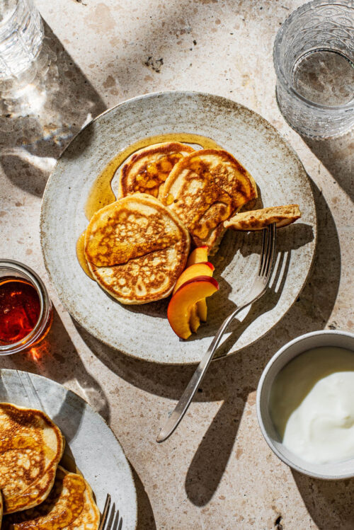 Small pancakes on a plate with fruit and maple syrup.