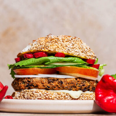 A bean burger patty on a seed bun with tomatoes, lettuce, and hot pepper.