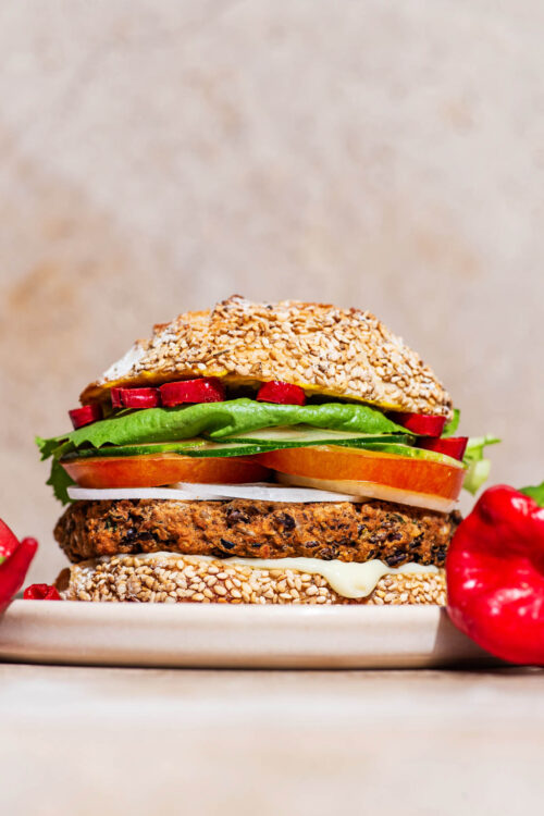 A bean burger patty on a seed bun with tomatoes, lettuce, and hot pepper.