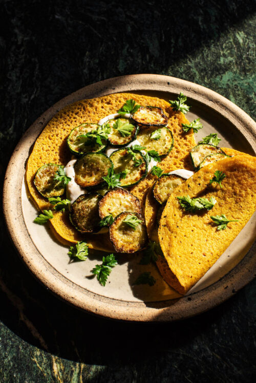 Two thin pancakes on a plate filled with yogurt, zucchini, and herbs.