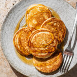 A plate with five pancakes topped with maple syrup.