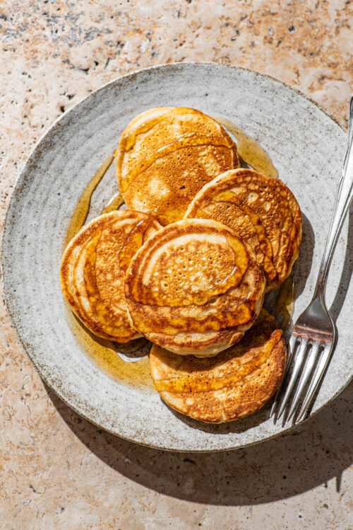 A plate with five pancakes topped with maple syrup.