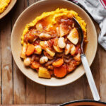 A shallow bowl with a light orange mashed pumpkin base topped with bean vegetable stew.