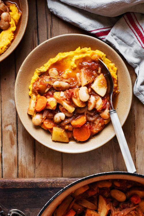 A shallow bowl with a light orange mashed pumpkin base topped with bean vegetable stew.