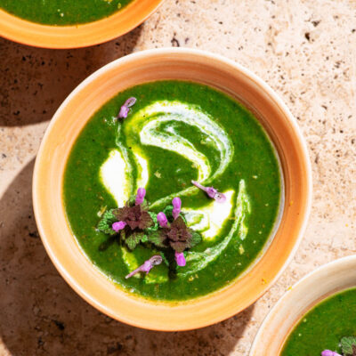 Three bowls of vivid green soup with a cream swirl and small purple flowers.