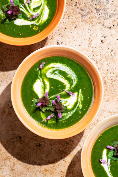 Three bowls of vivid green soup with a cream swirl and small purple flowers.