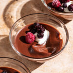 Three small glass bowls filled with chocolate pudding, garnished with cream and berries.