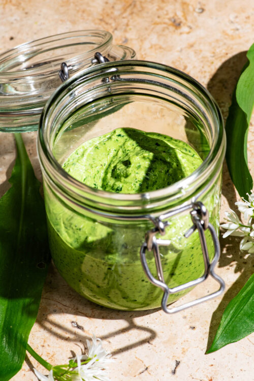 A flip-top jar filled with a green sauce, wild garlic leaves around.