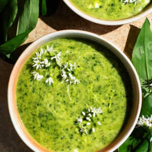 Two shallow bowls filled with green soup, topped with small white flowers.