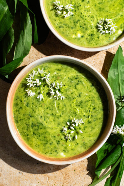 Two shallow bowls filled with green soup, topped with small white flowers.
