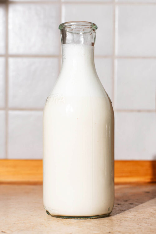 A glass bottle of nut milk on a kitchen counter.