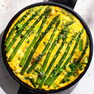 Frittata topped with asparagus spears in a round cast iron pan.