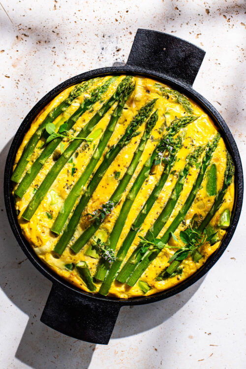 Frittata topped with asparagus spears in a round cast iron pan.