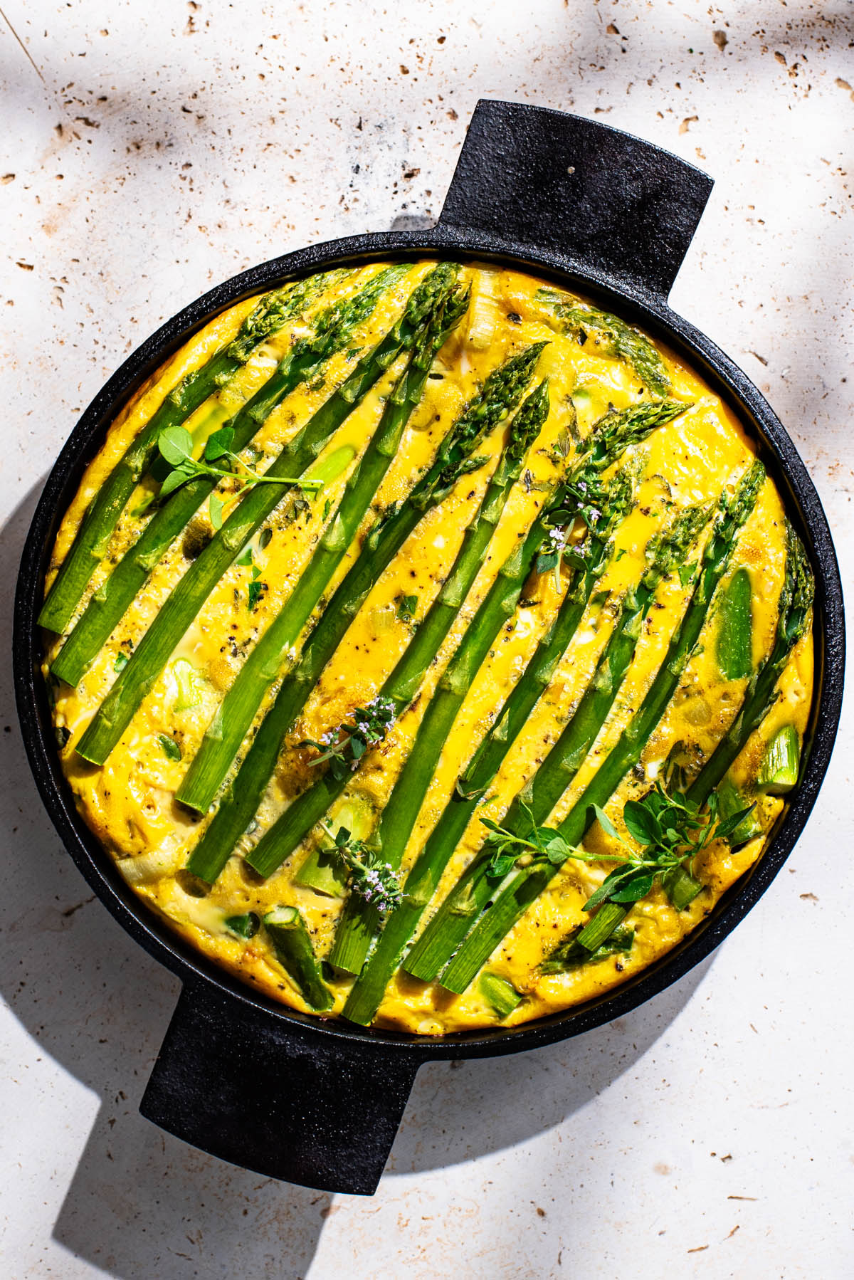 Frittata topped with asparagus spears in a round cast iron pan.