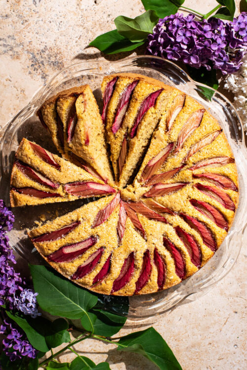 A rhubarb-topped cake with three slices cut, each on a slight angle.