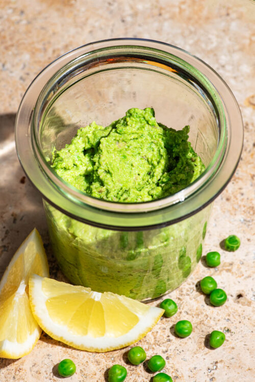 A light green spread in a glass jar, with lemon and peas in front.