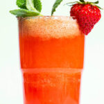 Close-up of a glass filled with a pink drink, garnished with mint and a strawberry.