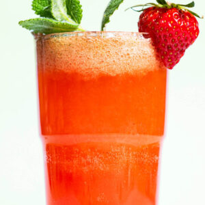 Close-up of a glass filled with a pink drink, garnished with mint and a strawberry.