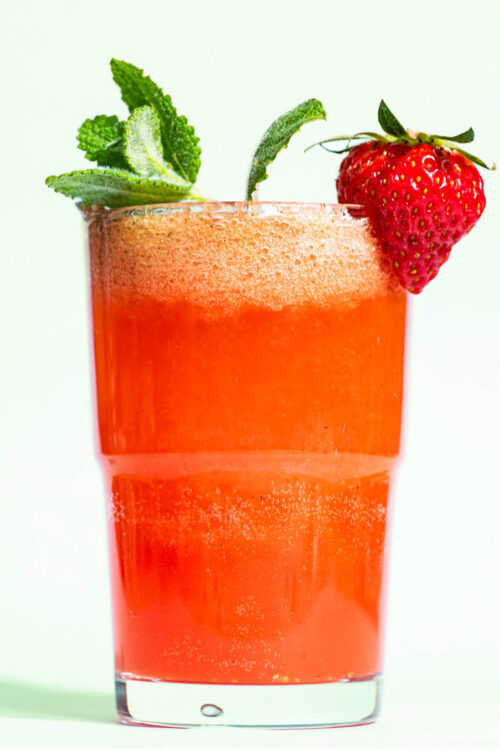 Close-up of a glass filled with a pink drink, garnished with mint and a strawberry.