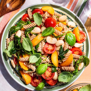 A large plate of short pasta with cherry tomatoes, white beans, basil, and apricots.