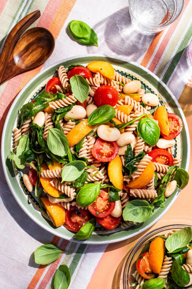 A large plate of short pasta with cherry tomatoes, white beans, basil, and apricots.
