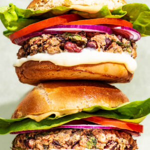 Two bean burgers with tomatoes, lettuce and onion, stacked on top of each other.