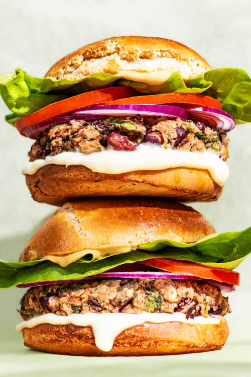 Two bean burgers with tomatoes, lettuce and onion, stacked on top of each other.