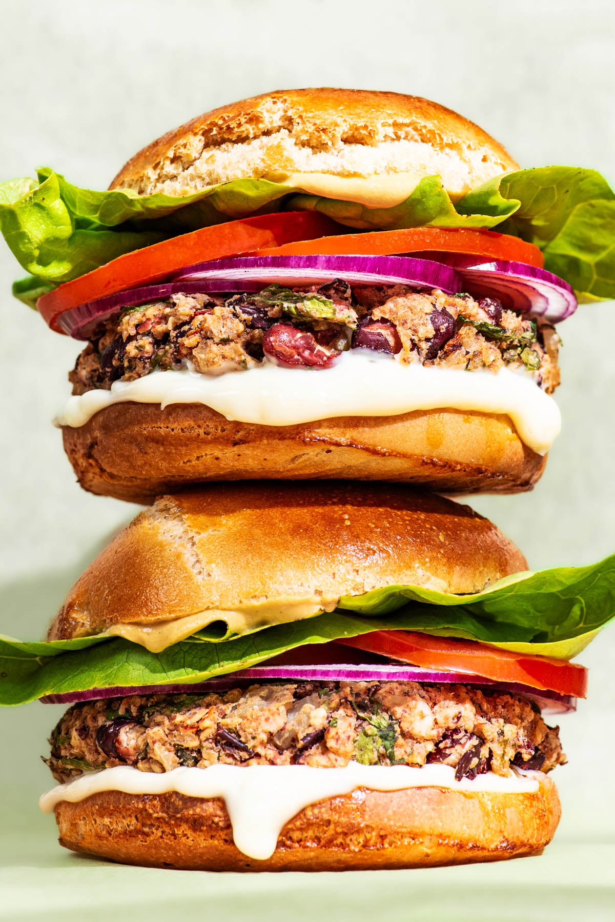 Two bean burgers with tomatoes, lettuce and onion, stacked on top of each other.