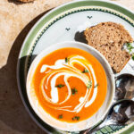 A bowl of orange soup swirled with cream and topped with thyme.
