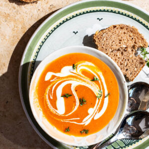 A bowl of orange soup swirled with cream and topped with thyme.