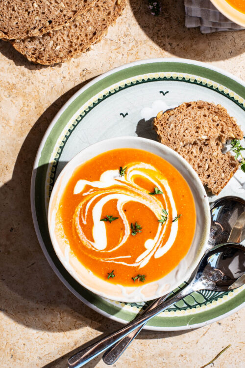 A bowl of orange soup swirled with cream and topped with thyme.