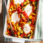 Four baked eggs in a rectangular baking dish with summer vegetables.