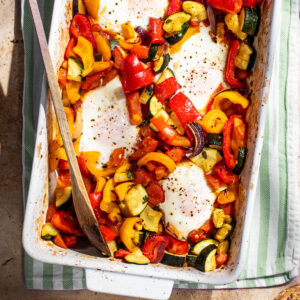 Four baked eggs in a rectangular baking dish with summer vegetables.